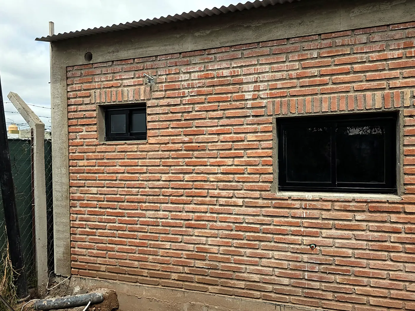Pared de ladrillo visto con un ventiluz y una ventana corrediza de aluminio negro